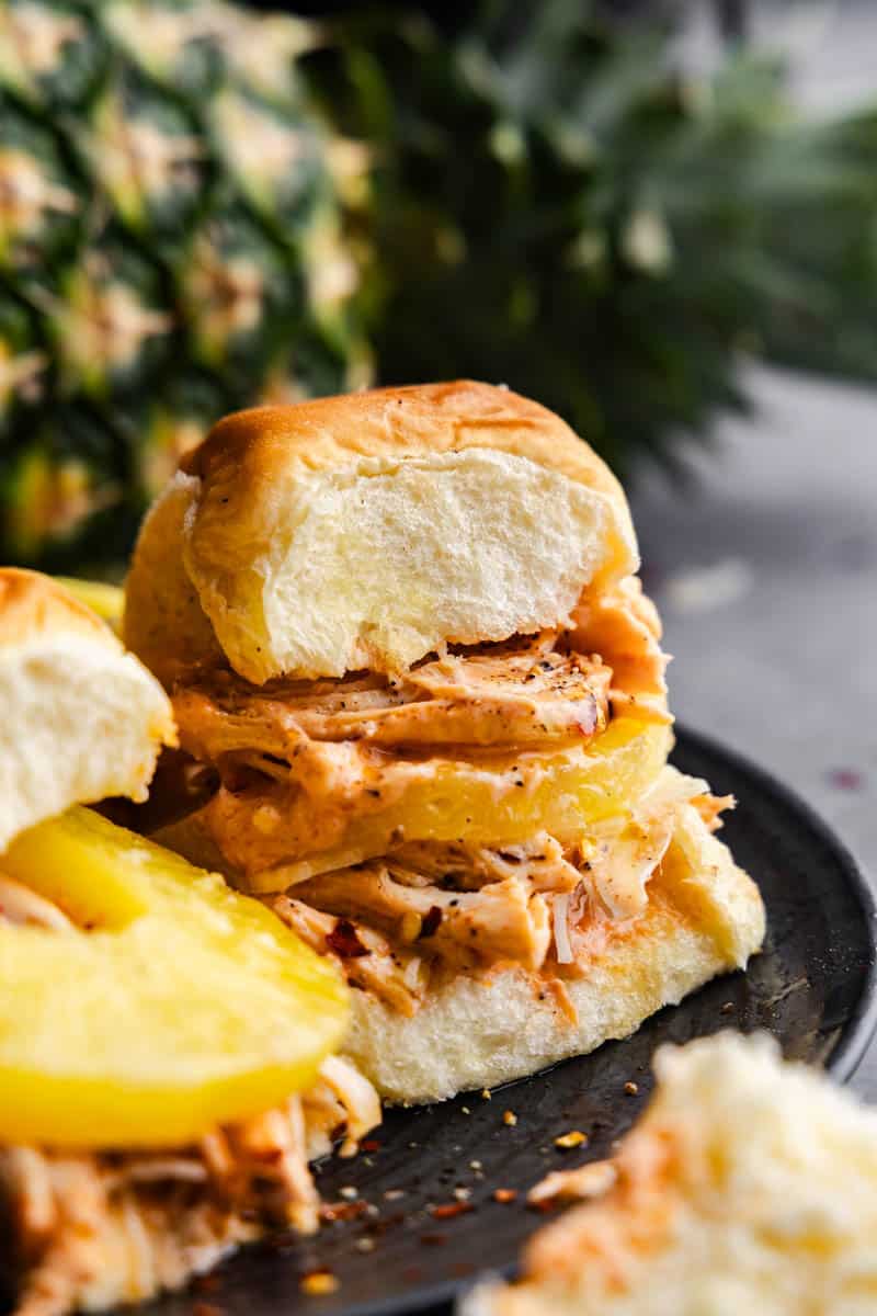 A close up view of a cream cheese chicken slider with pineapple on a plate.
