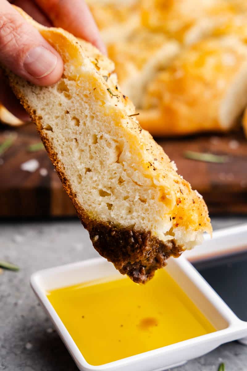 A slice of rosemary focaccia being dipping into oil and vinegar.