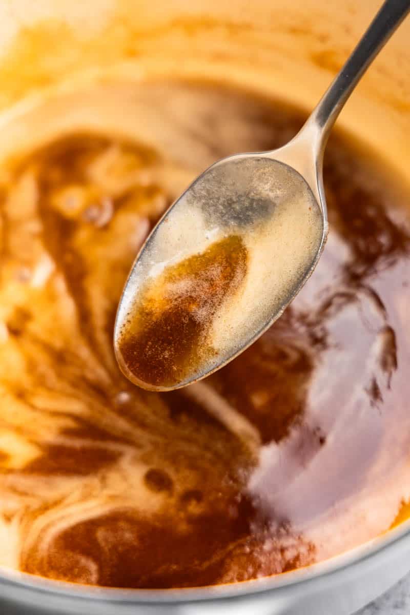 A spoon holding brown butter, swirling over a saucepan with brown butter.