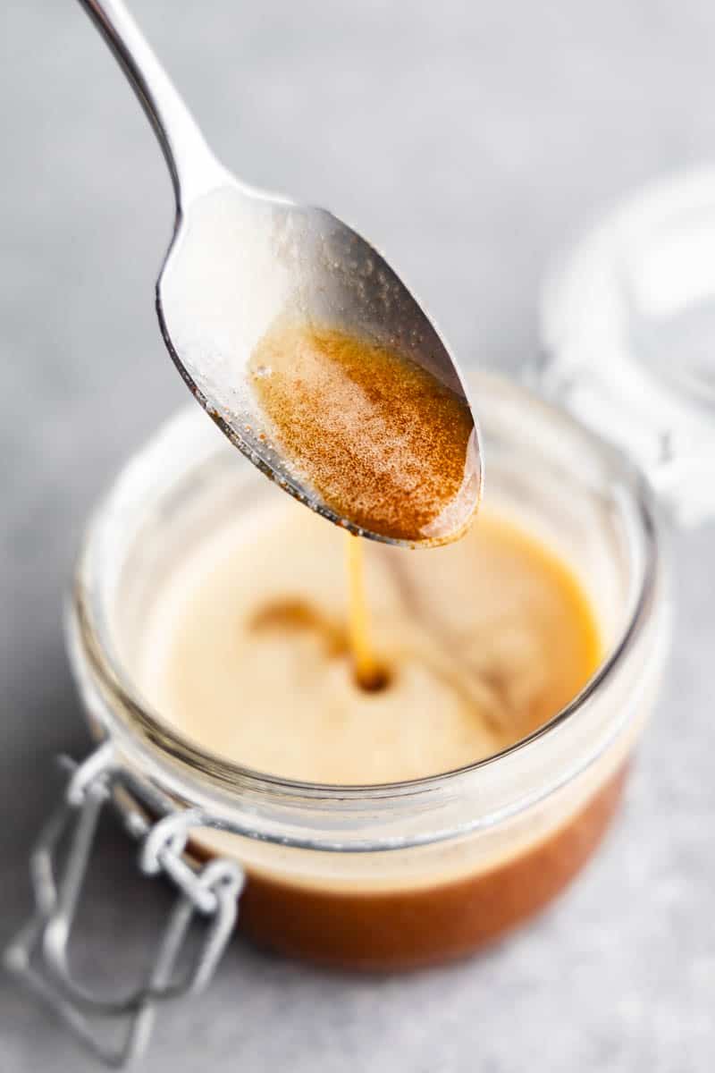 A jar filled with browned butter with a spoon scooping some out of the jar.