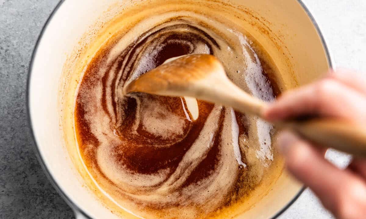 A top view of a saucepan with browned butter, being stirred with a wooden spoon.