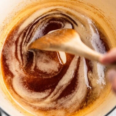 A top view of a saucepan with browned butter, being stirred with a wooden spoon.