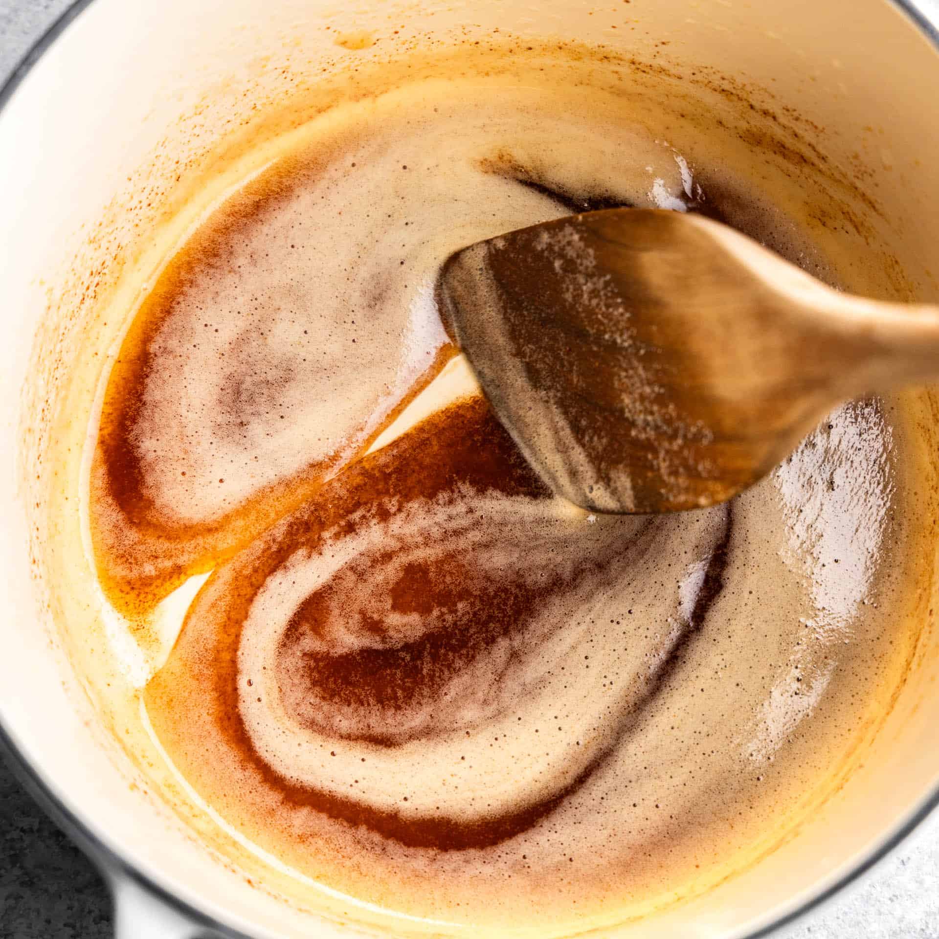 A top view of a saucepan with browned butter being stirred with a wooden spoon.