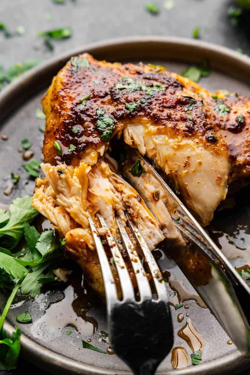 A Mexican-spiced chicken thigh in a plate with a fork and knife cutting into it to show the juicy meat inside.