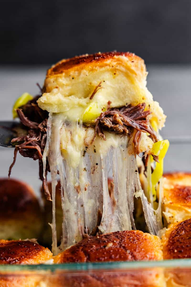 A gooey cheesy Mississippi Pot Roast Slider being lifted out of the pan.