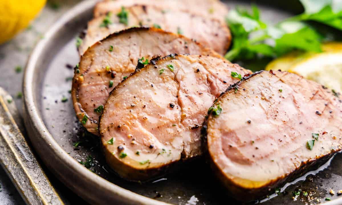 Slices of cooked pork tenderloin are arranged on a plate.