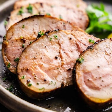 Slices of cooked pork tenderloin are arranged on a plate.