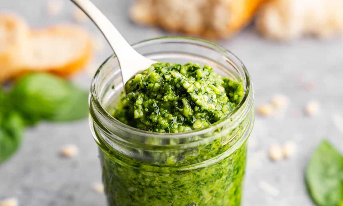 A small glass jar and a spoon of basil pesto.