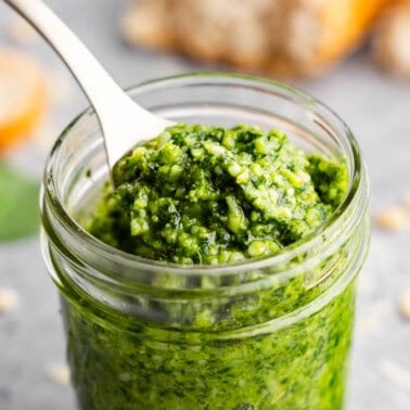 A small glass jar and a spoon of basil pesto.