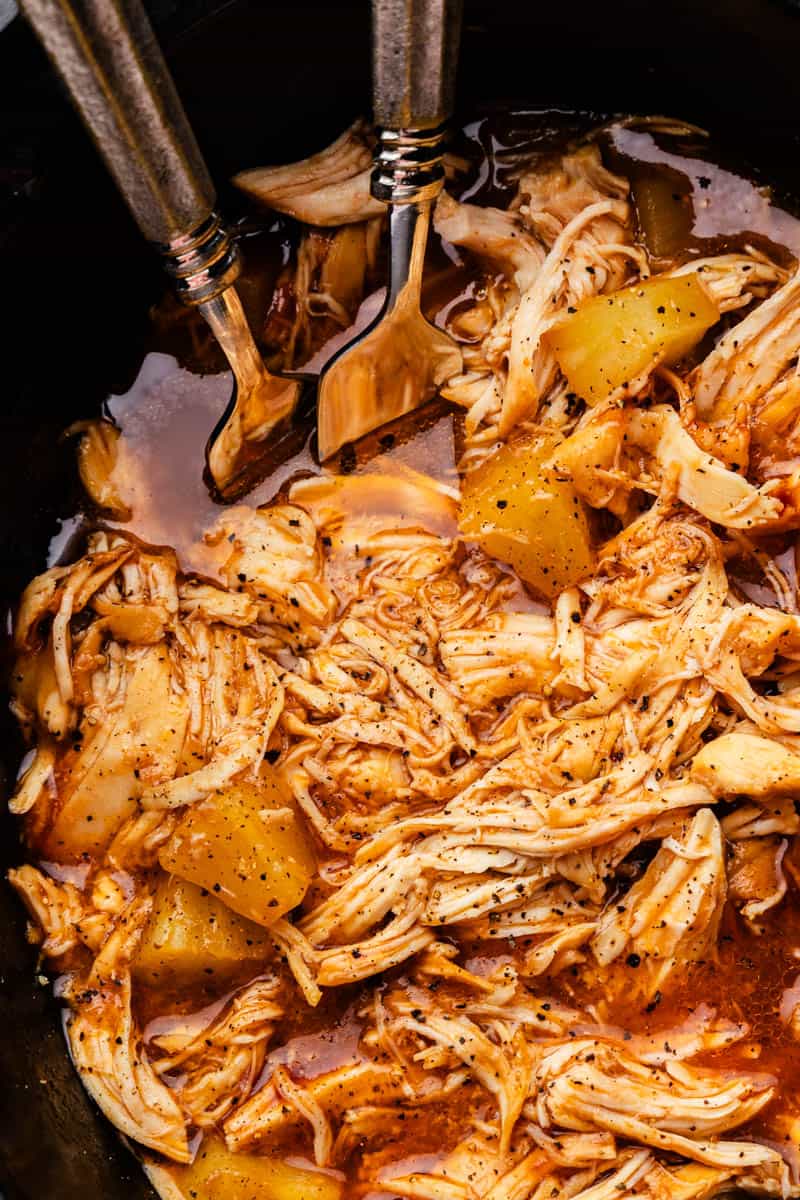 A close up view into a slow cooker filled with shredded BBQ chicken and pineapple juices.