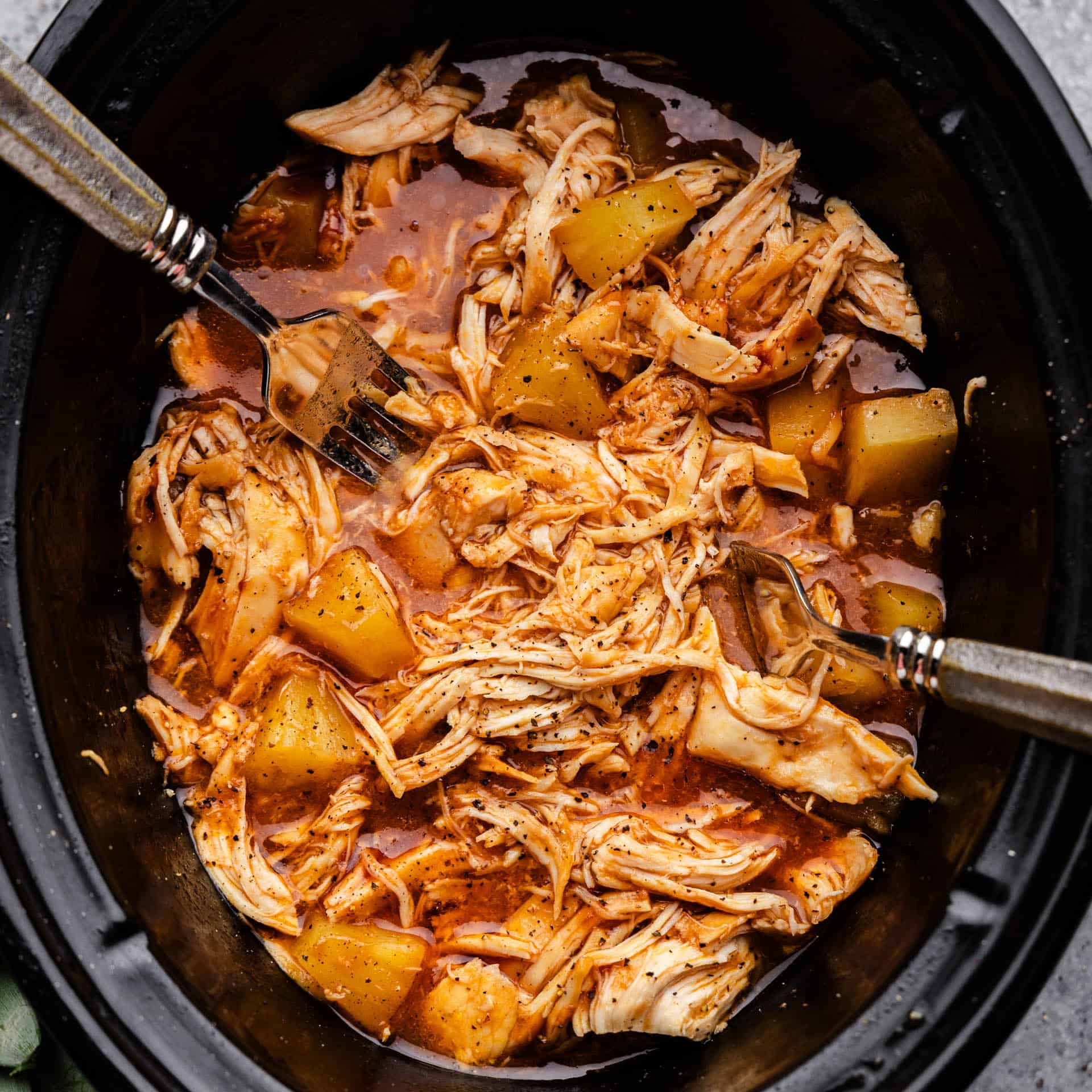 An overhead view looking into a slow cooker full of shredded chicken in a homemade BBQ sauce with pineapple.