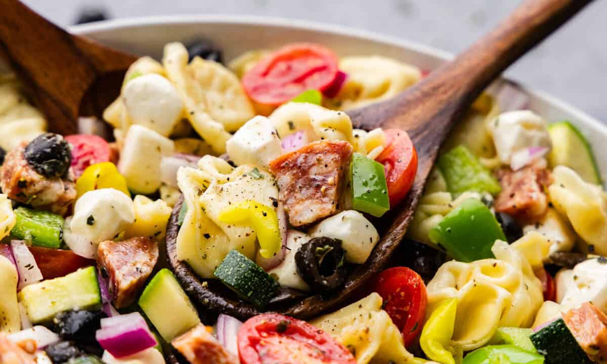 A large bowl of tortellini pasta salad with with a wooden serving spoon.