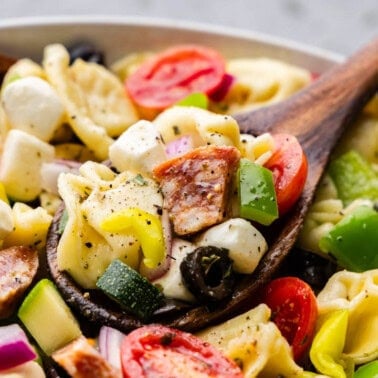 A large bowl of tortellini pasta salad with with a wooden serving spoon.