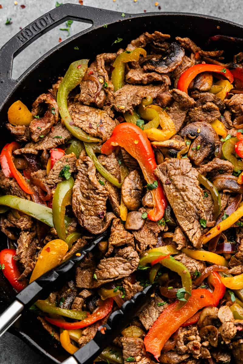 A close up of strips of cooked steak and colorful bell peppers cooked together.