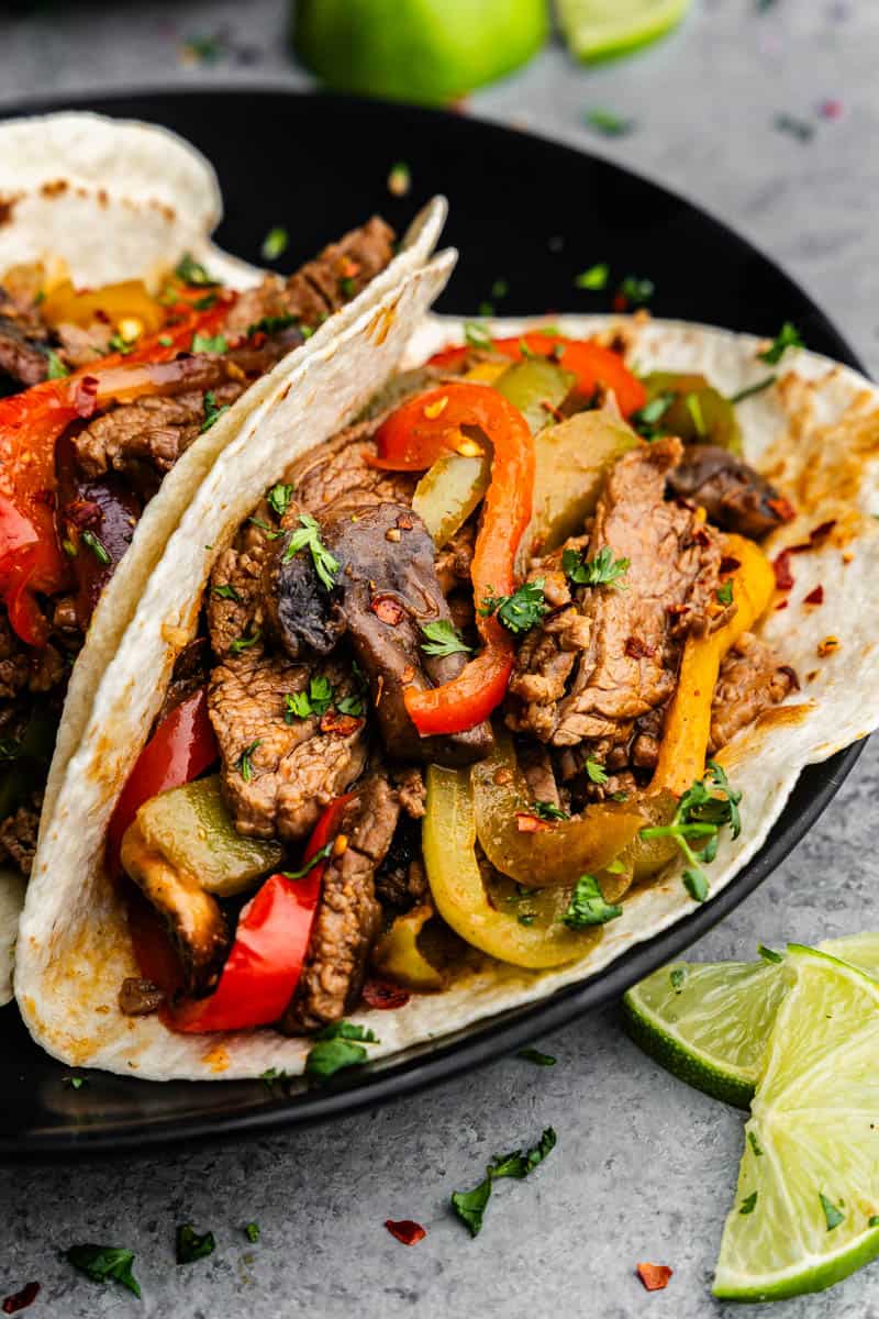 A close up of flour tortillas filled with steak fajitas on a plate.