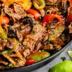 An angled view of a cast iron skillet filled with steak fajitas.