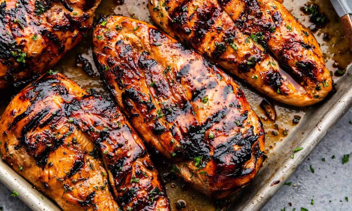 Several perfectly grilled and golden chicken breasts on a baking sheet.