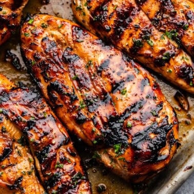 Several perfectly grilled and golden chicken breasts on a baking sheet.