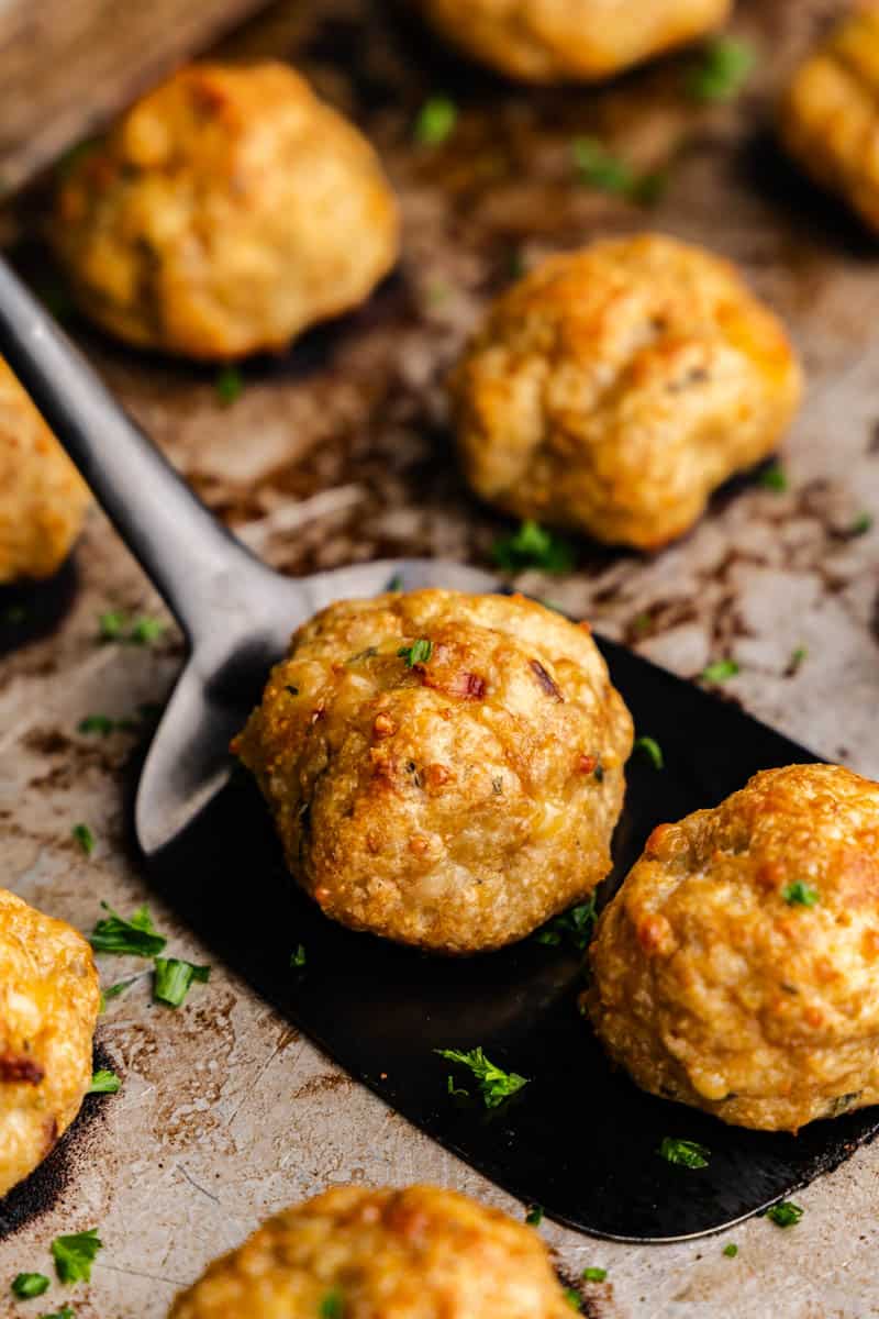 A spatula is lifting the baked chicken meatballs from the baking sheet.