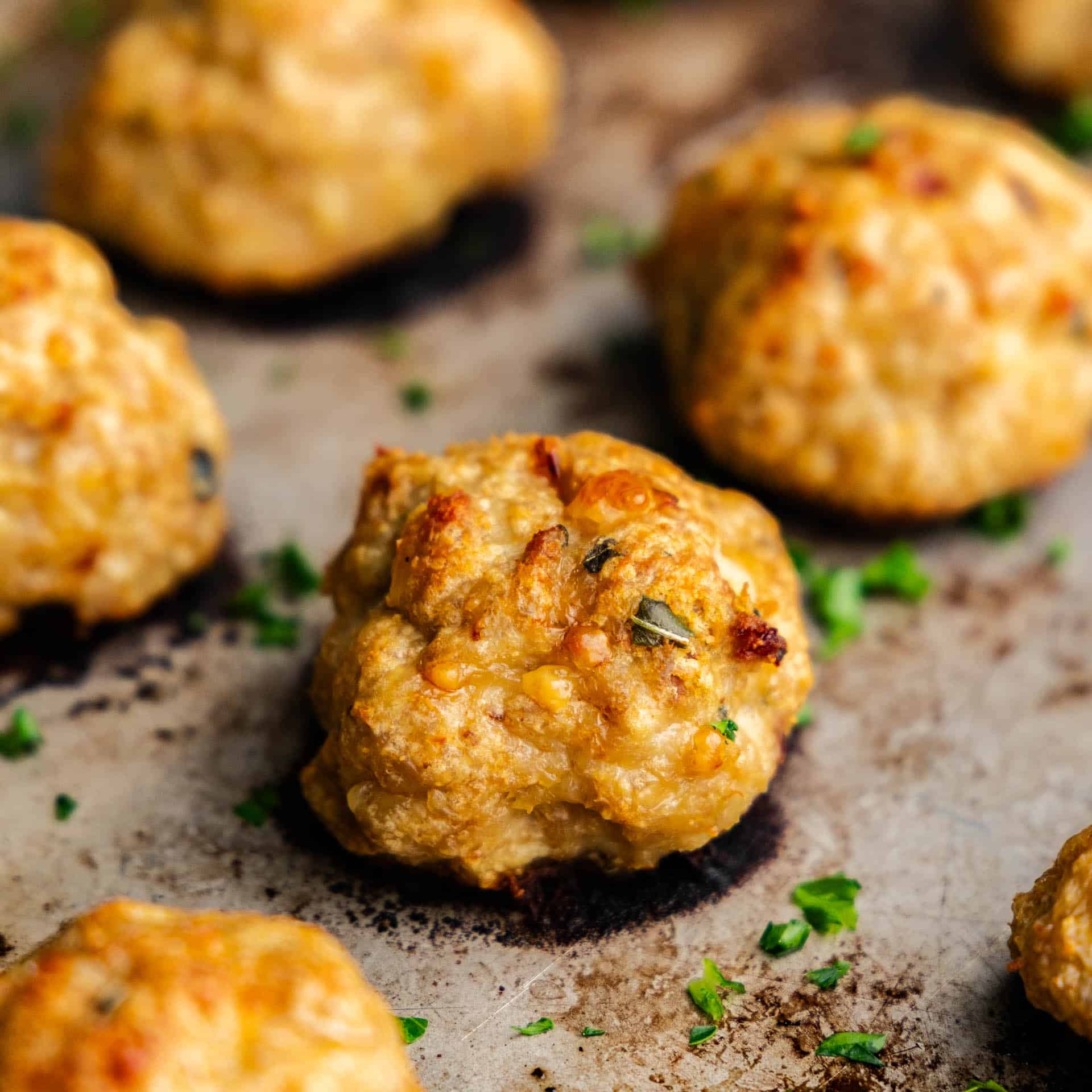 A close up of baked chicken meatballs on a metal baking sheet.