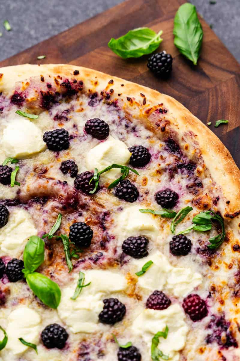 An uncut blackberry basil ricotta pizza, with all the fresh toppings on display.