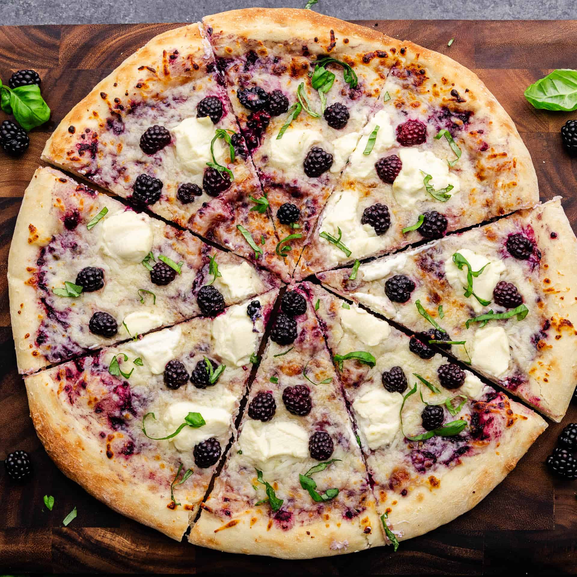 Looking overhead at a whole blackberry basil ricotta pizza with a few slices having been cut.