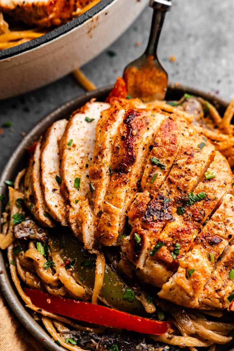 A plate filled with spaghetti noodles and bell peppers, topped with a piece of chicken breast