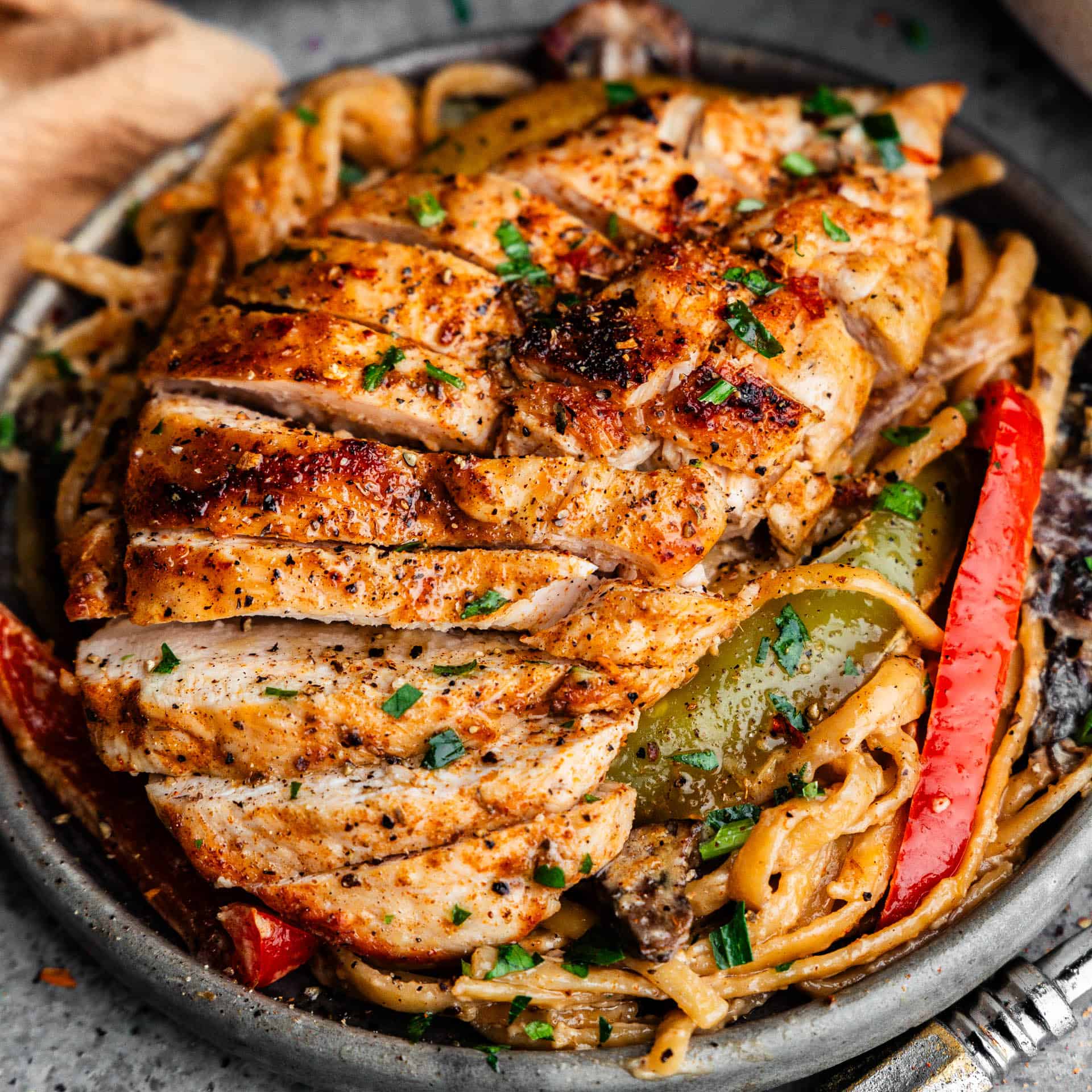 A skillet filled with a sliced chicken breast on top of noodles and bell peppers.