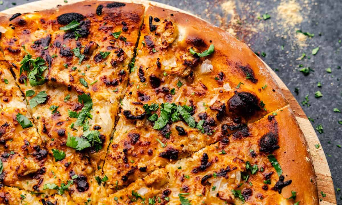 An overhead shot of a corner of a tikka masala chicken pizza with a slice cut and ready to take.