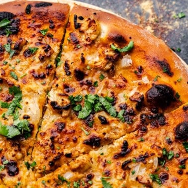 An overhead shot of a corner of a tikka masala chicken pizza with a slice cut and ready to take.