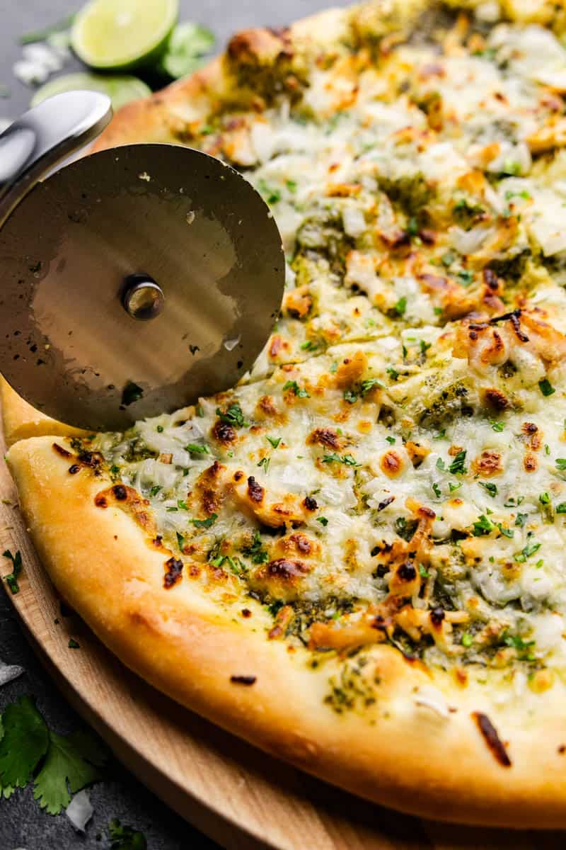 A close up of a pizza slicer cutting a line through cilantro lime pizza.