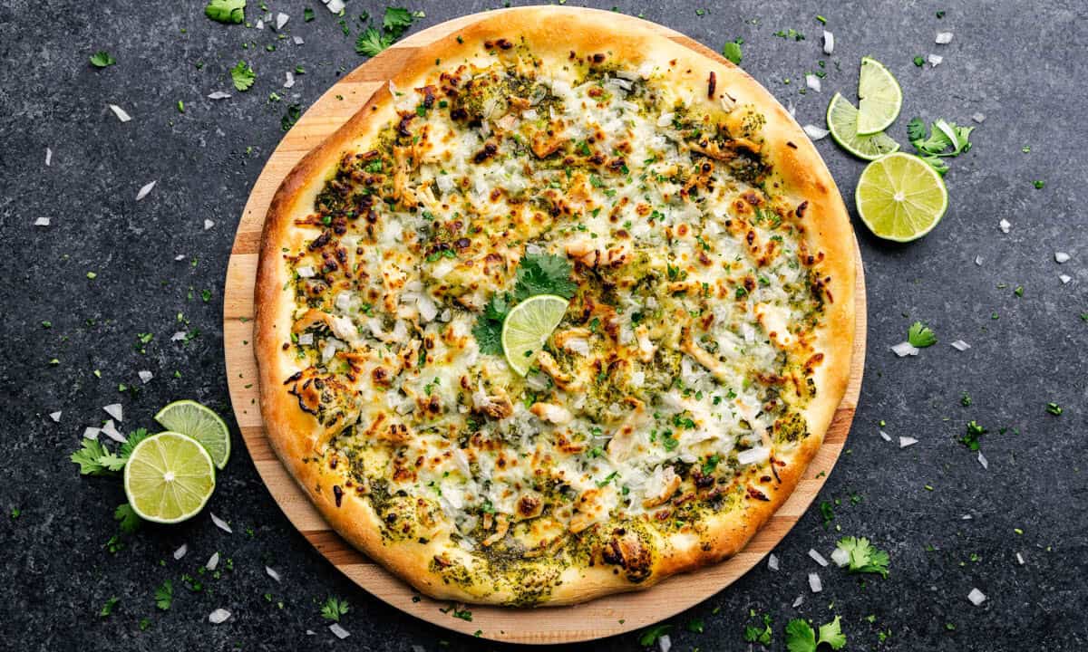 An overhead shot of a full uncut pizza covered in white cheese and green toppings, with fresh limes.