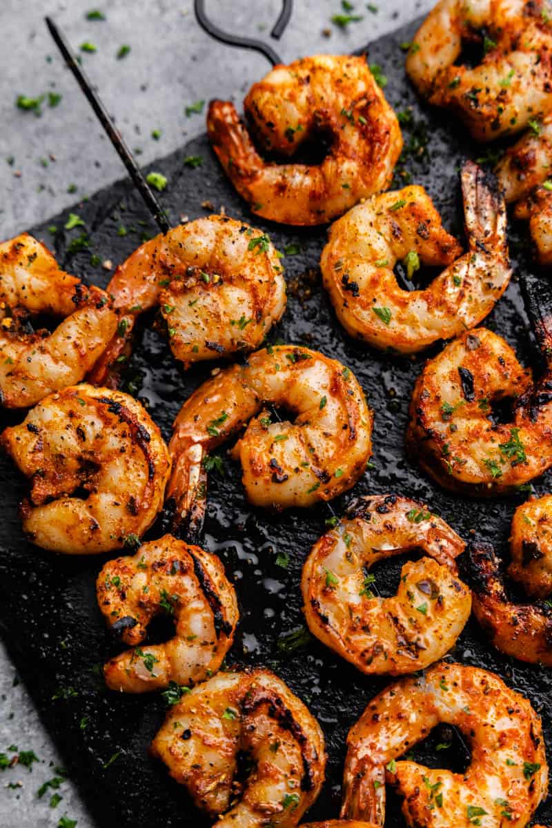 Overhead view of grilled shrimp on a skewer sitting on a black serving platter.