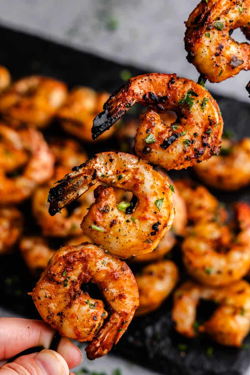 A close up view of a skewer of grilled shrimp with more in the background.