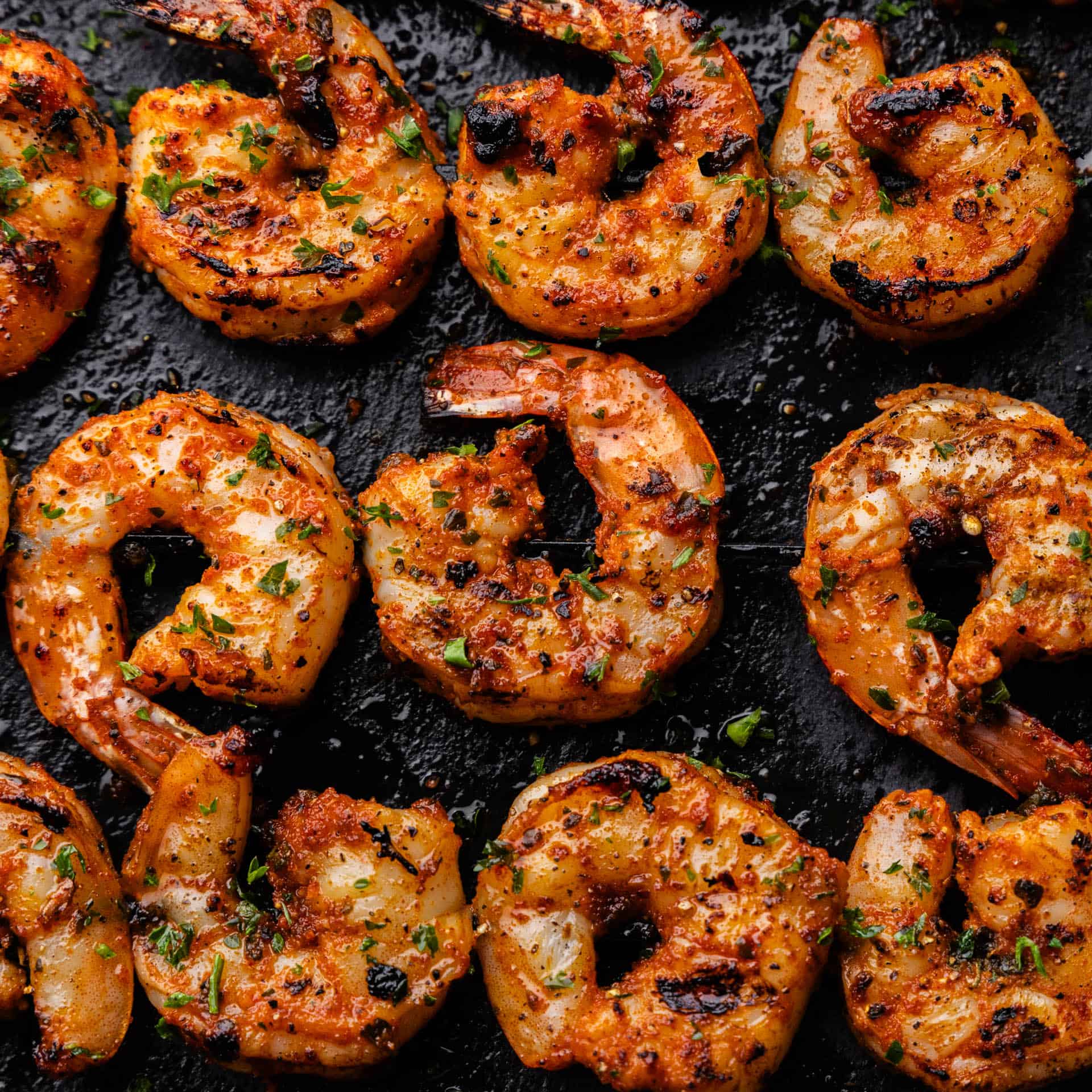 An overhead view of grilled shrimp on skewers sitting on a black serving platter.