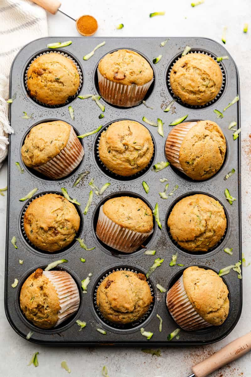 An overhead shot of a cupcake pan with golden brown zucchini muffins with some set skew in the pan.