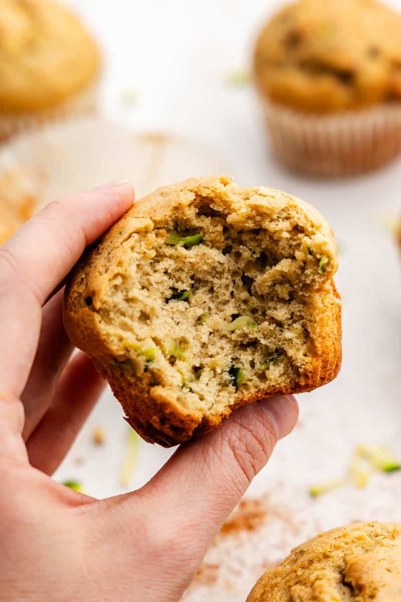 A hand holding a zucchini muffin with a large bite taken out of it.