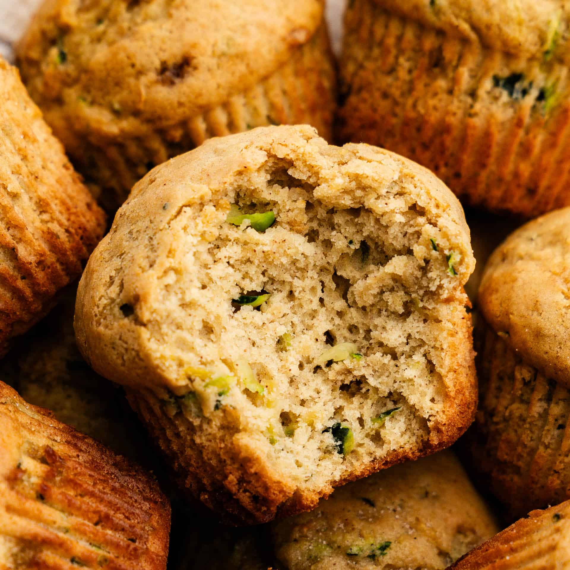 A close up shot of a pile of zucchini muffins with the focus of the one in the middle with a large bite taken out of it.