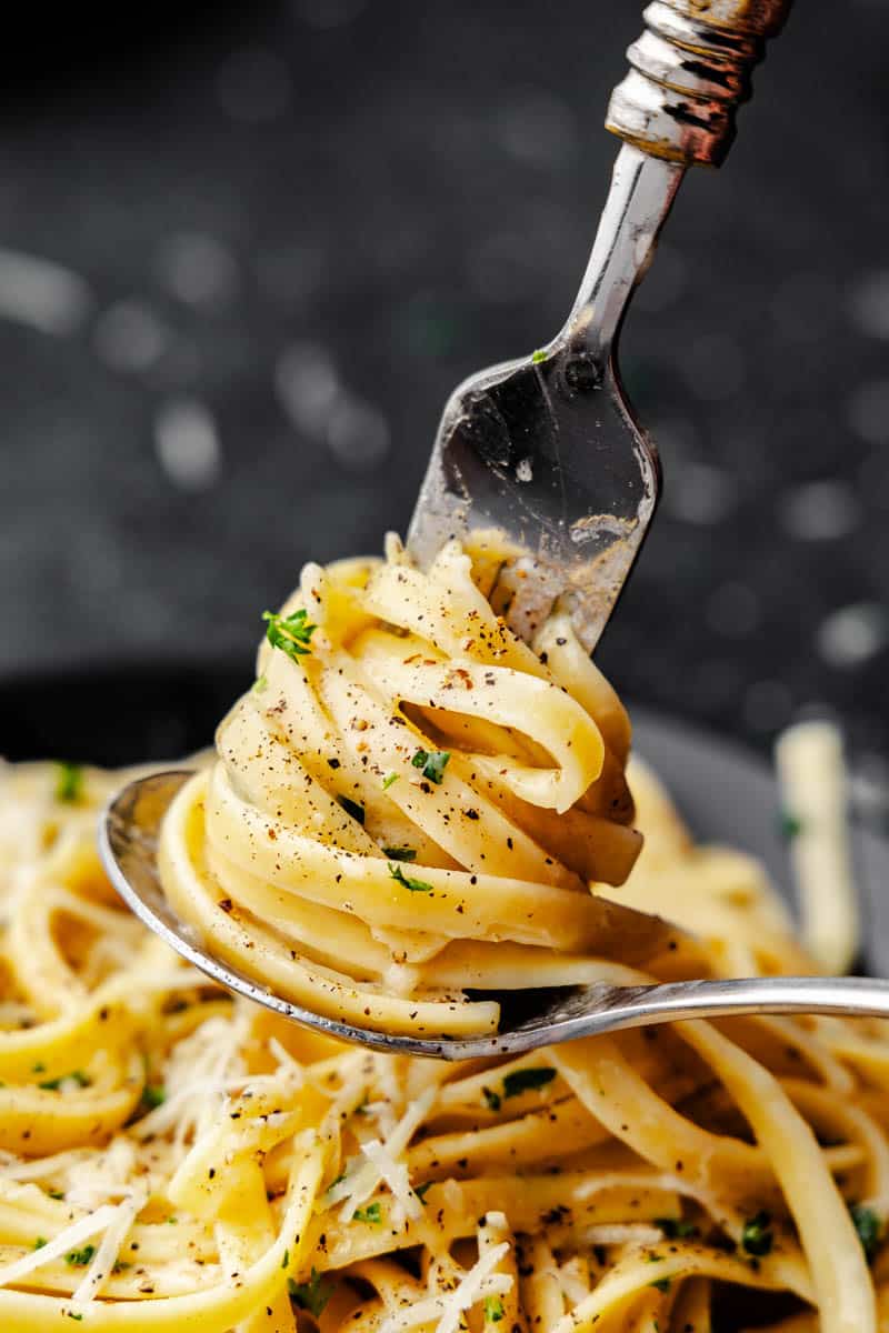 A fork with fettuccini alfredo swirled around it using a spoon to help keep the fettuccine on the fork.