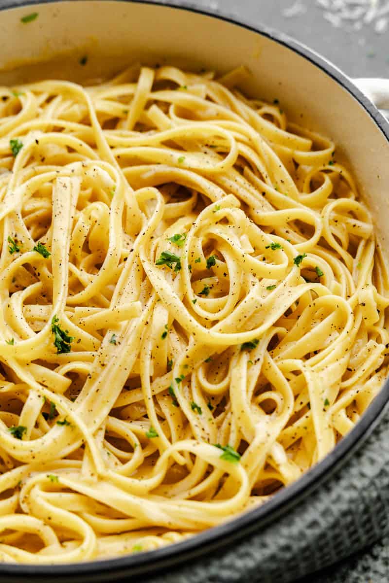 A pot filled with creamy fettuccine alfredo and topped with fresh parsley.