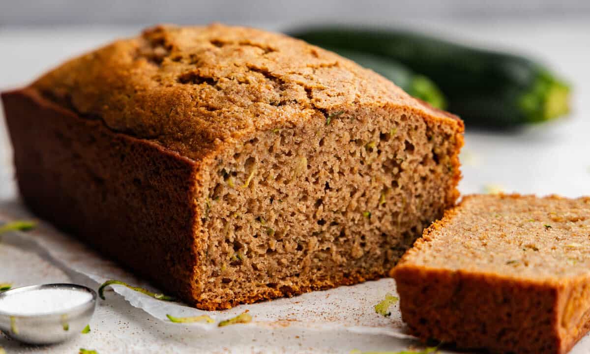 A loaf of zucchini bread with a slice cut off and laying in front of it.