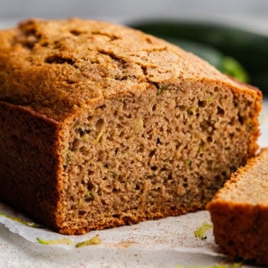 A loaf of zucchini bread with a slice cut off and laying in front of it.