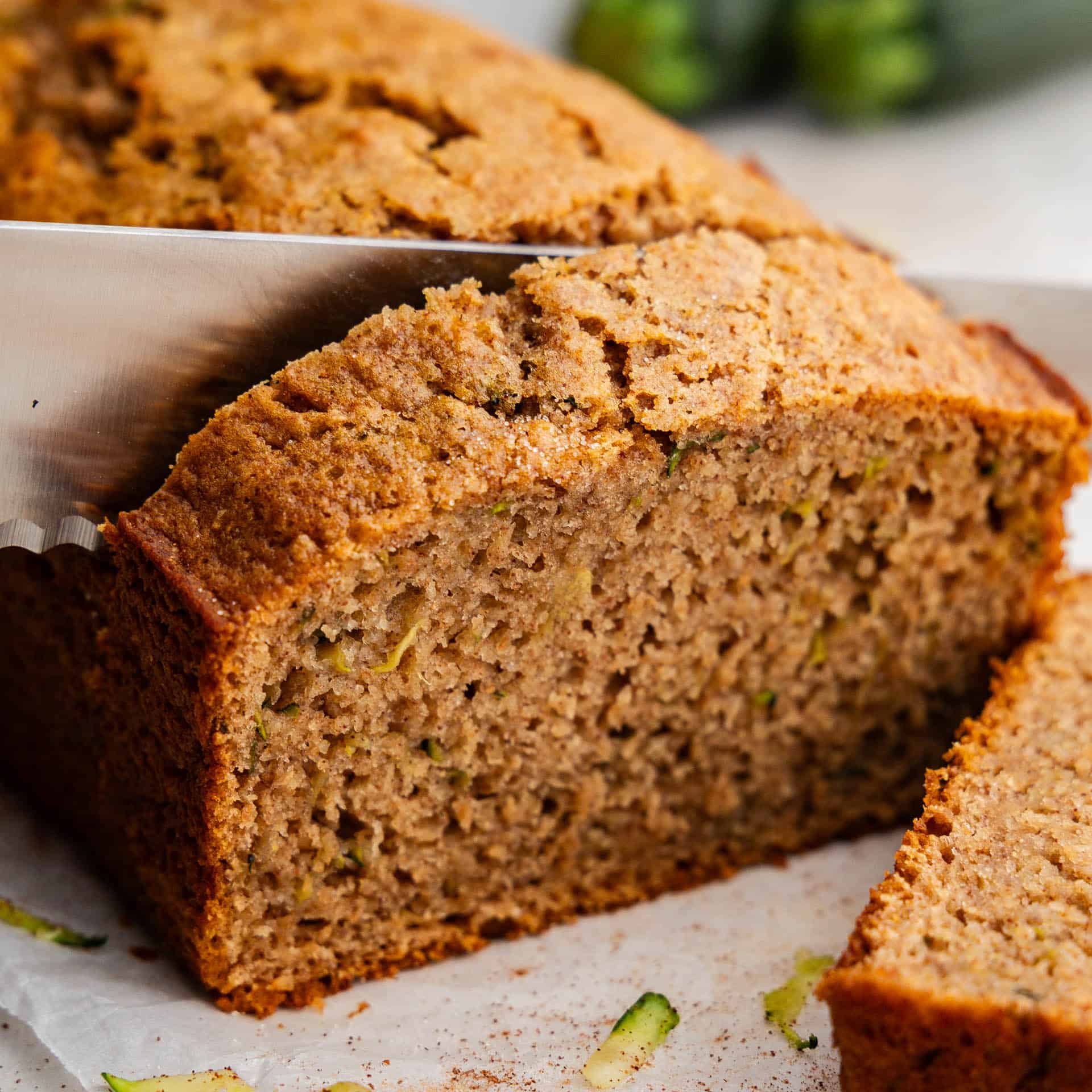 A close up shot of a loaf of zucchini bread being sliced with a knife, with one piece already cut and laying down.