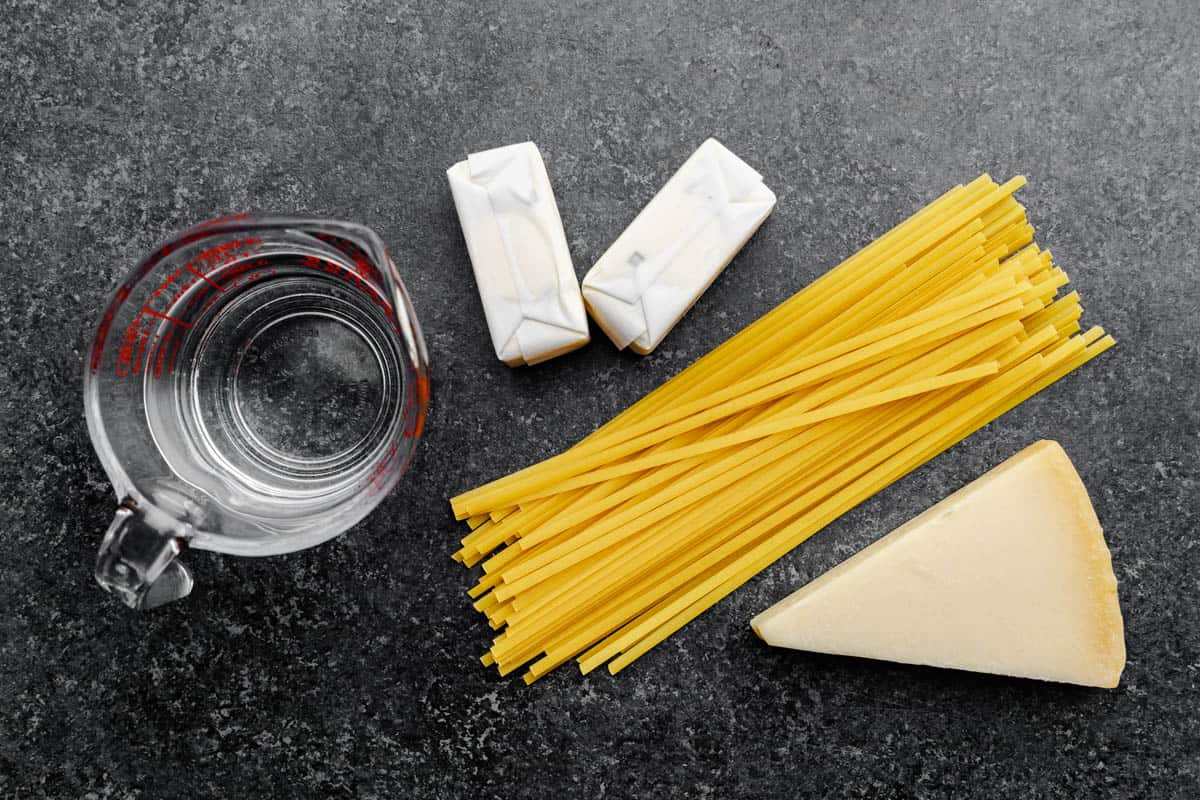 An overhead shot of dry fettuccine noodles, butter and parmesan cheese and a measuring cup.