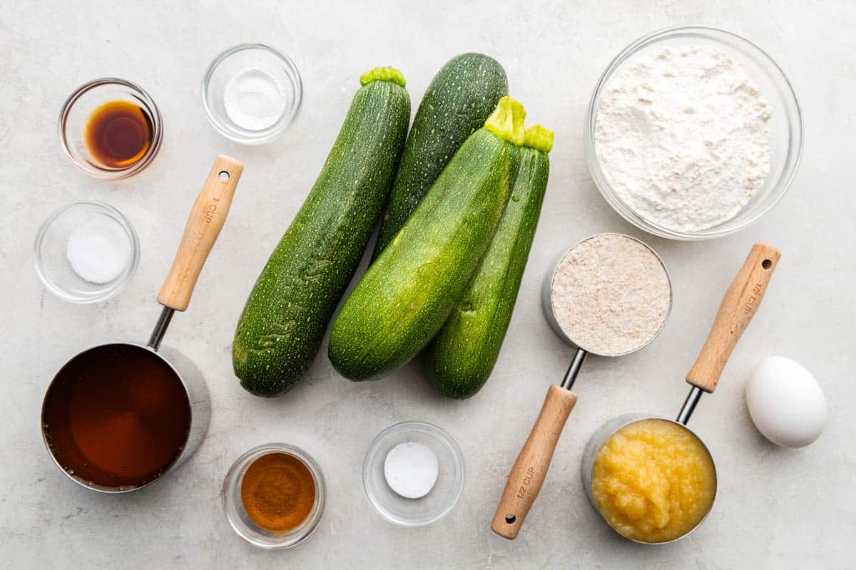 An overhead shot of whole zucchinis surrounded by measuring cups and spoons filled with ingredients.