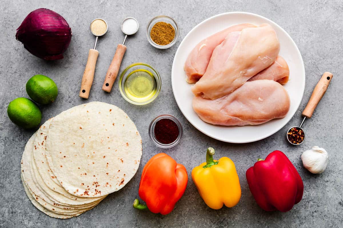 An overhead shot of raw, wet and dry ingredients for making chicken fajitas.