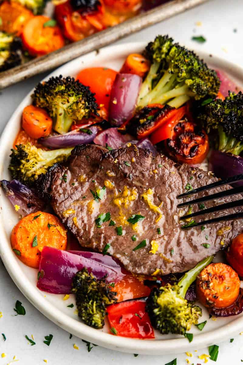 Overhead closeup view of steak on a plate surrounded by colorful vegetables.