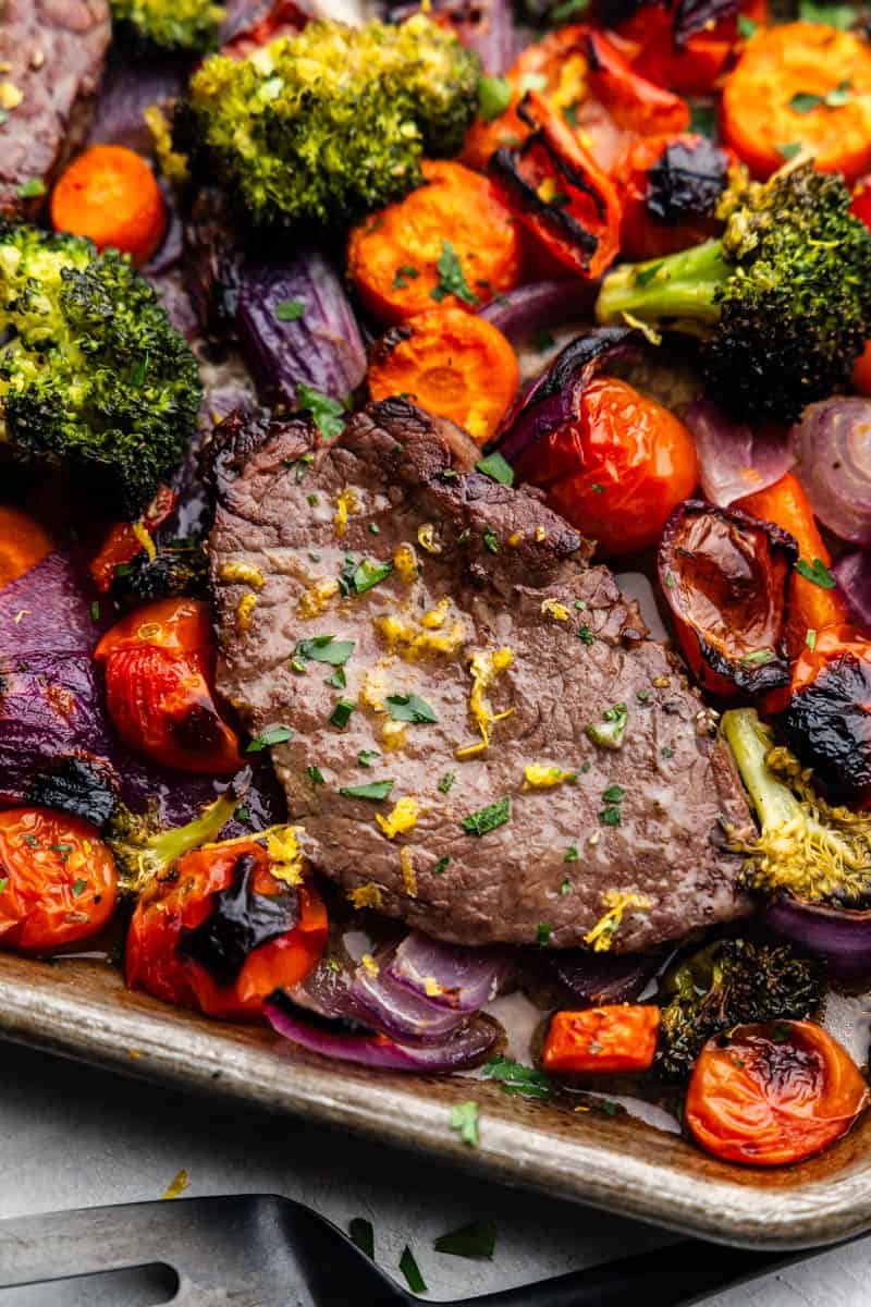 An overhead view of steak on a sheet pan surrounded by roasted vegetables.