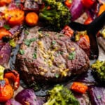 A close up view of a steak on a sheet pan surrounded by roasted vegetables.