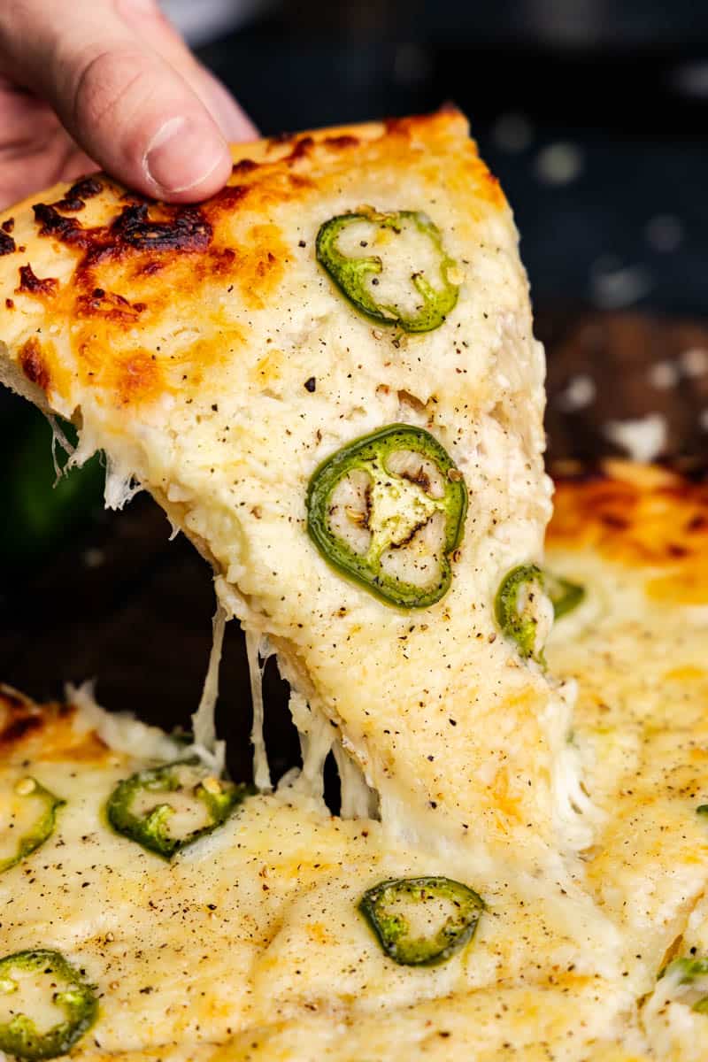 A close up of a slice of Jalapeno Scalloped Potato Pizza being pulled from the rest of the pie with cheese stretching.